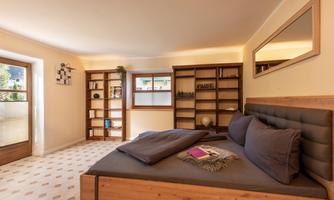 A modern bedroom with a large bed and cozy pillows. In the background, wooden shelves and a window are visible.