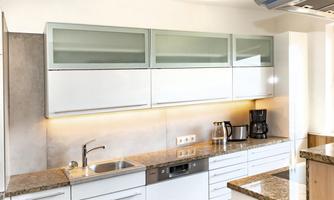 A modern kitchen with white cabinets and a granite countertop. In the background, a window and a coffee machine are visible.