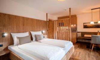 Bright, modern living/sleeping area with double bed, warm wooden furniture, and cozy seating area.