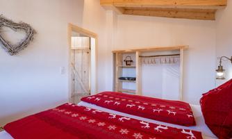 A cozy bedroom with two single beds and red bedspreads. The room has wooden details and a warm-hearted atmosphere.