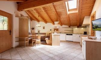 A bright, modern kitchen with a beamed wooden ceiling and tiled floor. The space is well furnished with a dining table and cozy seating options.
