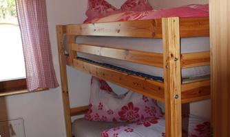 A simple room with a wooden bunk bed. The bedding has a floral pattern in pink and white.