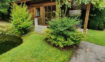 A cozy wooden house surrounded by green nature. A small pond and well-maintained plants give the place a peaceful atmosphere.