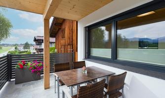 A cozy balcony with a table and chairs. In the background, green landscapes and a clear sky can be seen.