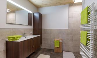 A modern bathroom with a wooden ceiling and bright tiles. The equipment includes a sink, a mirror, and fresh towels in bright green.