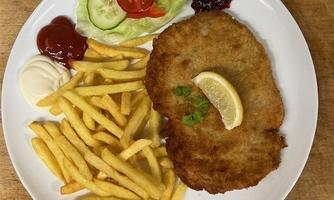 A plate with breaded schnitzel, French fries, and fresh salad. It comes with ketchup, mayonnaise, and lingonberry jam.