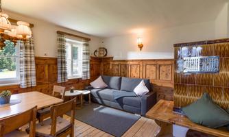 A cozy living space with wooden furniture and a gray sofa. The room has large windows and a rustic charm.