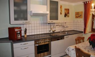 A modern kitchen with bright cabinets and stainless steel appliances. The table is decorated with a white tablecloth and a red floral arrangement.