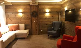 A modern living room with wooden walls and cozy furniture. A light beige sofa and a gray armchair are in the room, complemented by a bright red armchair.