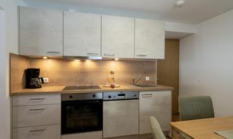 A modern kitchen with light cabinets and a wooden countertop. It is well equipped with a stove, oven, and coffee machine.