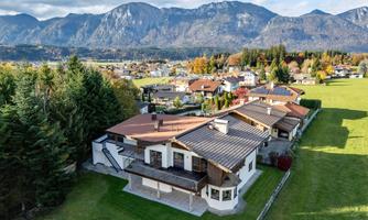 An attractive residential area with modern houses and a large garden. In the background, impressive mountains and a clear sky stretch out.