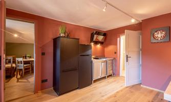A modern kitchen with a black refrigerator and a stainless steel stove. The walls are painted in a warm red tone, and the floor is made of wood.