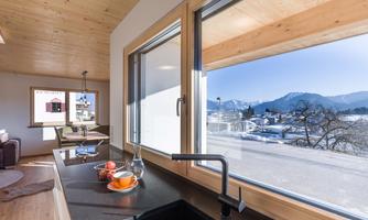 A modern kitchen with a view of the mountains and the winter landscape. Bright windows and wooden details create a cozy atmosphere.