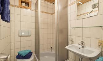 A modern bathroom with a shower cubicle and a sink. The walls are tiled and there are towels in fresh colors ready.