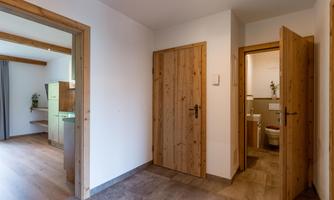 A bright hallway with wooden doors and a modern, minimalist design. On the left side, there is an access to a kitchen, while the right door leads to a bathroom.