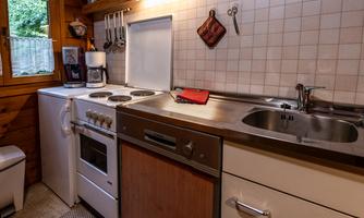 A small, well-equipped kitchen with a stove, a sink, and a washing machine. The wooden decor and the window create a cozy atmosphere.