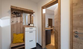 A modern entrance area with a light wooden cabinet and a mirror.  
The walls are painted in neutral colors, and the floor is tiled with dark tiles.