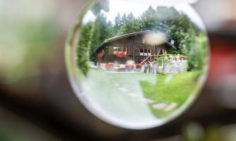 A cozy wooden cabin surrounded by trees. The focus is on the cabin, viewed through a lens.