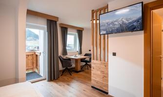 Modern furnished room with dining area, wall-mounted TV, and balcony with stunning views of the mountains.