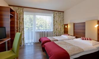 A cozy hotel room with two single beds, a desk, and a television. Large windows let in plenty of daylight and offer a view of the surroundings.