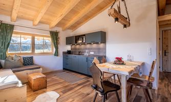 A cozy vacation apartment with wooden beams and a modern kitchen area. The space is bright and inviting, with a dining table and a seating area.