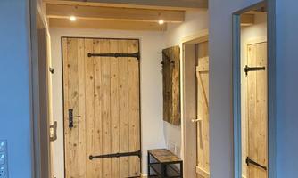 A bright hallway with a wooden front door and a large mirror. The floor is made of wood, and there is a small bench in the corner.