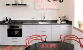 A modern kitchen with white cabinets and a dark countertop. Red chairs around a round table complement the elegant design.