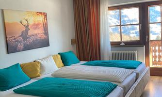 A cozy bedroom with two beds and colorful pillows. Large windows provide plenty of daylight and a view outside.