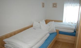A simple bedroom with two beds and bright walls. There is striped bedding and a window with curtains.