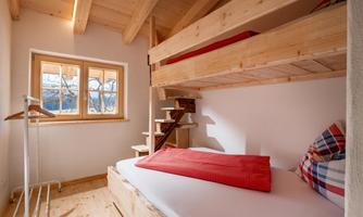 A cozy bedroom with wood decor and a loft bed. Soft light falls into the room through the window.