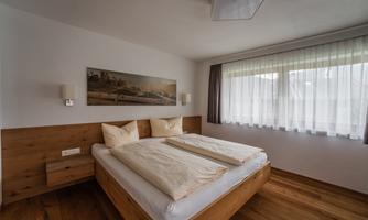 A modern bedroom with a double bed and bright wood interiors. Large windows let in plenty of daylight.