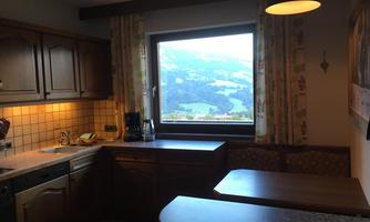 A cozy kitchen with wooden cabinets and a large window. The view shows a picturesque mountain landscape.
