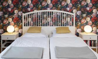 A modern bedroom with two beds and a blooming pattern on the wall. Each bedside table has a stylish lamp.