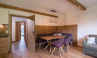 Bright and modern dining room with a large wooden table and comfortable chairs. An open door leads to another room that is simply furnished.