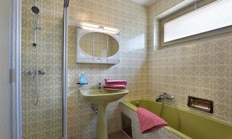 A bathroom with green tiles, a bathtub, and a shower. Pink towels are laid on the sink.