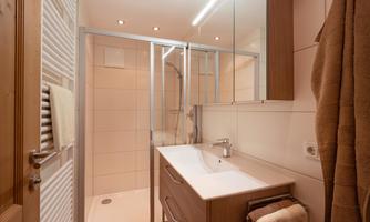 A modern bathroom with a glass shower and a wooden vanity. The walls are in light colors and there is warm lighting.