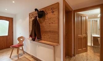 An inviting entrance area with wooden furniture and a coat rack. To the right, a bathroom can be seen, while a chair and a doormat complement the space.