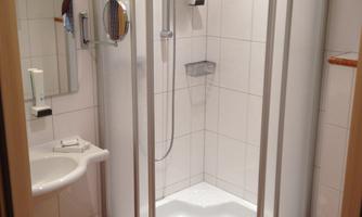 A modern bathroom with a shower cubicle. There is a washbasin and a toilet, all in light colors.