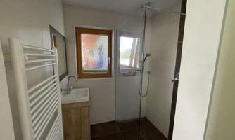 A modern bathroom with a shower and a sink. Large windows provide natural light.