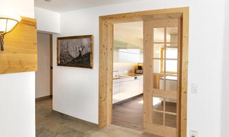 A bright hallway with wood paneling and a glass door leading into a modern kitchen. A picture hangs on the wall, decorating the space.