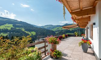 A beautiful terrace with blooming plants and a magnificent view of the green mountains. The sky is clear and the atmosphere is relaxed.