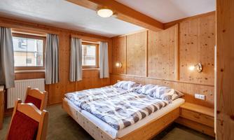 A cozy bedroom with a double bed and wood paneling. The windows let in daylight and the decor is rustic and inviting.