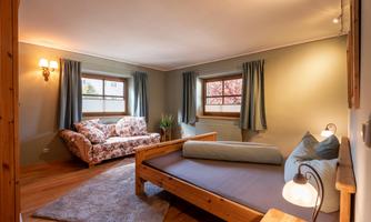 A cozy room with a wooden bed and a comfortable sofa. The walls are painted in soft colors, and large windows allow for plenty of daylight.