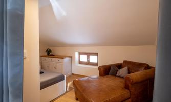 A cozy room with a comfortable couch and a bed. Light streams through a window, creating an inviting atmosphere.