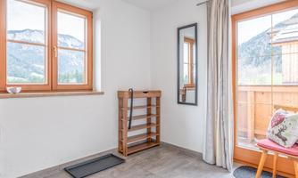 A bright interior with large windows and a view of the mountains. A wooden shelf and a chair are in the room, which radiates a cozy atmosphere.