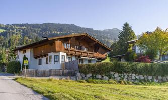 A typical chalet in a picturesque mountain landscape. The surroundings are green with many trees and a clear sky in the background.