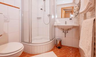 A modern bathroom with a shower, a sink, and a toilet. The walls are tiled, and the decor is bright and clean.