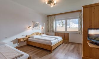 Bright bedroom with double bed, single bed, television, and large windows.