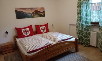 A cozy bedroom with a large double bed and red pillows. The room has a green curtain and a picture of mountains on the wall.
