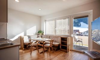 A bright studio with a dining table and chairs. Large windows offer a view of the garden.